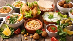 A bowl of creamy Chia Catering hummus topped with olive oil and chickpeas, surrounded by fresh vegetables and pita bread on a wooden table."